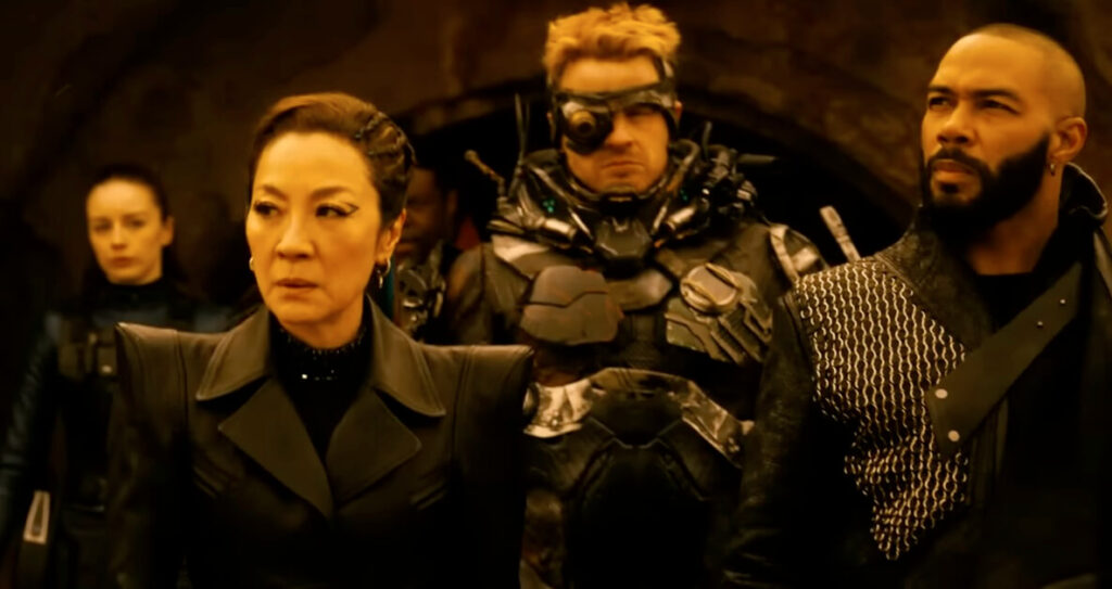 A serious-looking Philippa Georgiou, dressed in a sleek black outfit, stands in the foreground alongside two other characters. On her left is a man with futuristic armor and a cybernetic eyepiece, and on her right is a bearded man wearing a textured, asymmetrical uniform.